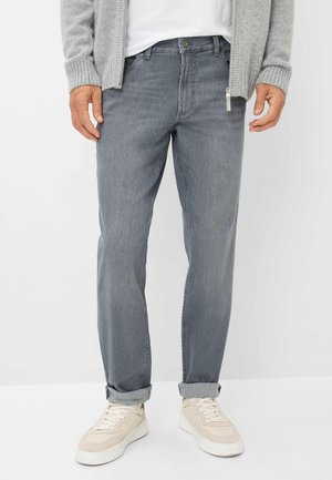 Jeans in denim grigio con taglio dritto, dotati di chiusura con zip e bottone, orli arrotolati e indossati con sneakers color crema.