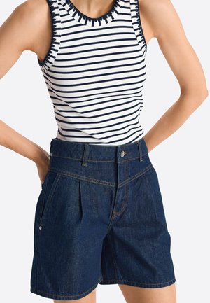 Person iført hvid ærmeløs top med marineblå striber og mørkeblå denimshorts med høj talje, forkant med folder og lommer.