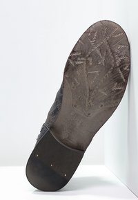 Suela de zapato de cuero marrón con un patrón texturizado, logotipo y fecha. El lado presenta un acabado liso con una ligera curva en el talón.