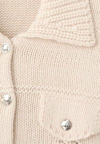 Cardigan de punto crema con diseño de cuello, botones plateados y costura texturizada. Detalle notable de bolsillo con solapa.