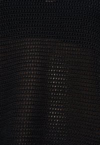 Sort hæklet stof med åbent strikmønster, der skaber et gitter af små huller, som viser hudtoner nedenunder.