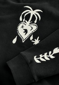Čierna mikina s vyšívanými bielymi motívmi, vrátane srdca s palmou, hviezd a vzoru listov na rukáve.