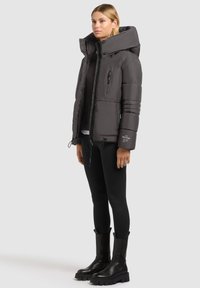 Vadderad grå pufferjacka med hög krage, blixtlås fram och sidfickor. Matchad med svarta leggings och kraftiga svarta ankelstövlar.