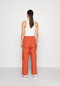 Orange cargobyxor med elastisk midja, som har sidfickor och en avslappnad passform, kombinerat med vita sandaler. Bakifrån vy av outfiten.