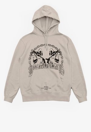 Jasnobeżowa bluza z kapturem z czarnym nadrukiem trzech wilczych głów w łańcuchowym okręgu oraz napisem „Nic nie jest większe niż karma” poniżej.