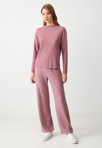 Różowy zestaw dzianinowy z długim rękawem, z teksturowanym wzorem zygzaka oraz dopasowanymi spodniami o szerokich nogawkach. Buty to białe sneakersy.
