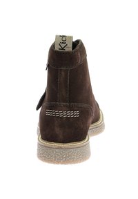 Botín marrón de ante hasta el tobillo con una superficie texturizada, suela de goma gris y una lengüeta en el talón. Presenta un detalle de costura blanca.