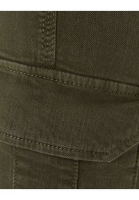 Olivgrön tyg med en texturerad yta, med en ficka med lock och diagonala sömdetaljer. Stark och hållbar material.