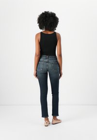 Zwart geribbeld tanktop, donkere skinny jeans met achterzakken en lichtgekleurde platte schoenen. Eenvoudig ontwerp, aansluitende pasvorm.