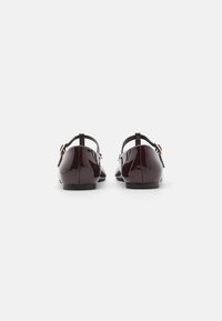 Chaussures en cuir verni bordeaux avec un dos ouvert, une sangle ajustable et une semelle en caoutchouc plate. Fini lisse et design minimaliste.