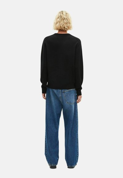Schwarzer Pullover mit Rundhalsausschnitt und langen Ärmeln, kombiniert mit lockeren blauen Jeans aus Denim, die über eine Rückentasche verfügen.