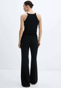 Black ribbed tank top paired with black, flared trousers. Material appears smooth, fitted at the waist, with minimal detailing.