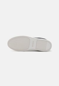 Svart sneaker med en texturerad gummisula med ett vågigt mönster och "HUGO"-logotyp, kompletterad av en slät övre design.