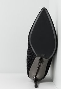Scarpa nera con tacco alto e punta affilata, esterno in stampa leopardata testurizzata e tacco metallico lucido. Suola nera liscia con marchio.