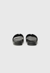 Black, flat sandals with an open toe design. Made of smooth material, featuring a minimalist look with a slight curve at the straps.