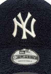 Casquette ajustable New Era 9FORTY bleu marine avec un logo NY brodé blanc bien en vue sur un tissu texturé. Étiquette de marque ronde visible.