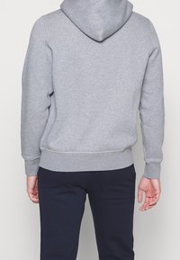 Grauer Hoodie mit einer geräumigen Kapuze, gerippten Bündchen und Saum, aus weichem Material gefertigt, kombiniert mit dunklen Hosen. Einfaches, klassisches Design ohne Muster.