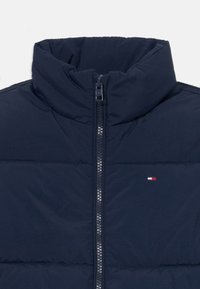 Chaqueta acolchada azul marino con un alto cuello, cremallera completa y costuras horizontales. Presenta un pequeño logotipo en rojo, blanco y azul.