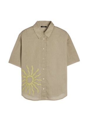 Koszulka z krótkim rękawem, z kołnierzykiem, w jasnobrązowym materiale z haftowanym żółtym słońcem na dolnym lewym rogu. Posiada guziki z przodu.