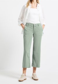 Světle zelené kalhoty culotte s předními kapsami, zapínáním na dva knoflíky a volným střihem. Nosené s bílým tílkem a béžovými teniskami.