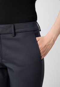 Tailored dark navy pants with a smooth, matte texture. Features a flat front, two side pockets, and a slim fit with a discreet waistband.