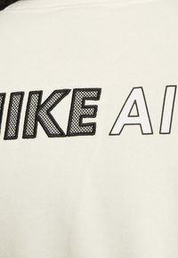 Sweatshirt blanc avec "NIKE" en maille noire en gras et "AIR" dans une police noire solide, présentant une finition lisse et texturée.