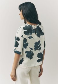 Floral print top in off-white with dark blue flower patterns, short sleeves, and a back keyhole opening. Soft, lightweight fabric.