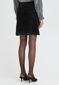 Zwarte kanten rok met gekartelde zoom, versierd met bloemenpatronen, gecombineerd met doorzichtige zwarte panty's en zwarte high-heeled slingback schoenen.