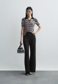 Kötött polo póló texturált, színes mintával, magas derekú fekete, cikkcakk mintás nadrággal és egy kis fekete-fehér geometrikus táskával párosítva.