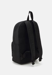Zaino nero con un'esterno liscio, schienale in rete imbottita, due spallacci regolabili e una tasca laterale con zip.