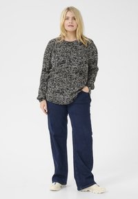 Top de manga larga en blanco y negro con un estampado, de corte relajado, combinado con pantalones de pierna ancha en azul oscuro y zapatos casuales de color claro.