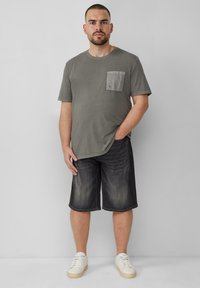 Szara bawełniana koszulka z kieszonką na piersi, w połączeniu z ciemnoniebieskimi szortami dżinsowymi i białymi trampkami. Prosty, casualowy design z krótkimi rękawami.