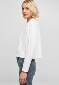 Weißes, kurzes Langarmoberteil mit lockerer Passform und Rundhalsausschnitt, kombiniert mit blauen Jeans. Einfaches Design, glatte Textur.