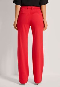 Felrood, wijde broek van zacht materiaal, met een gladde textuur, een aangesloten tailleband en twee achterzakken.