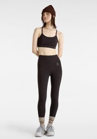 Svart sport-bh med justerbara remmar, matchad med högmidjade svarta leggings. Silverfärgade sömmar och ljusgrå träningssneakers.