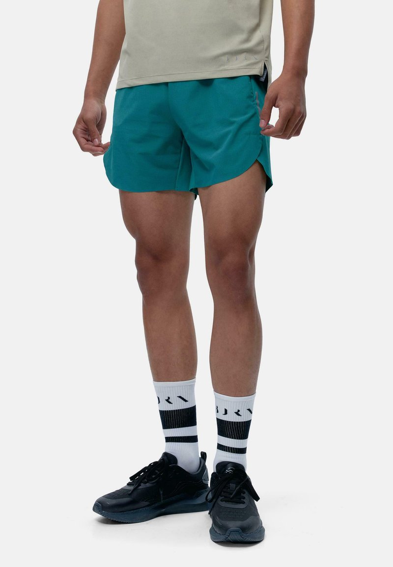 Teal træningsshorts i letvægtsmateriale med split-søm. Bruges sammen med sorte sneakers og hvide sokker med sorte striber.