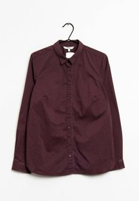Chemise bordeaux à manches longues sur un cintre, avec un col, une fermeture à boutons à l'avant et une texture de tissu lisse.