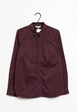 Burgunderfarbendes Langarmhemd an einem Kleiderbügel, mit einem Kragen, einer Knopfleiste und glatter Stofftextur.