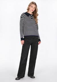 Pullover a righe blu navy e crema con un ampio colletto, tre bottoni e polsini a coste, abbinato a pantaloni neri a vita alta e a gamba larga.