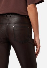 Bruine leren broek met een gladde textuur, een aansluitende pasvorm en achterzakken met subtiele stiksels en zilveren knoopaccenten.
