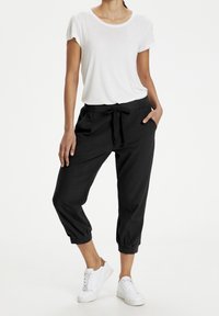 Bermuda hitam longgar dengan pinggang elastis dan tali serut. Dipasangkan dengan kaos lengan pendek putih berkerah bulat dan sneakers putih.