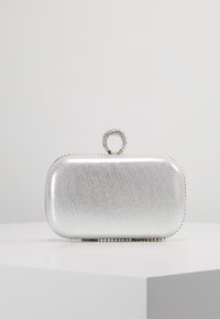 Pochette métallique argentée de forme rectangulaire, texture lisse, fermeture ronde ornée de strass, et bordure perlée le long du bas.