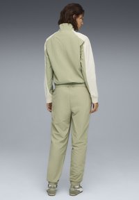 Lichtgroen trainingspak met witte mouwen, hoge kraag, elastische manchetten en tailleband. Gladde textuur; aansluitend ontwerp; minimalistische stijl.