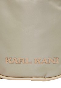 Borsa in nylon beige con logo "KARL KANI" in rilievo di colore beige chiaro. Texture liscia con forma strutturata e sottile motivo orizzontale.