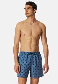 Blå badshorts med ett palmträdsmönster, tillverkade av lättviktig material. Har en elastisk midja med snörning för justerbar passform.