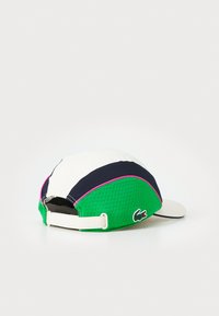Boné com um design estruturado, com painéis brancos, verdes e azuis-marinho. Textura em rede, pormenores em rosa, faixa ajustável e detalhe do logótipo na lateral.