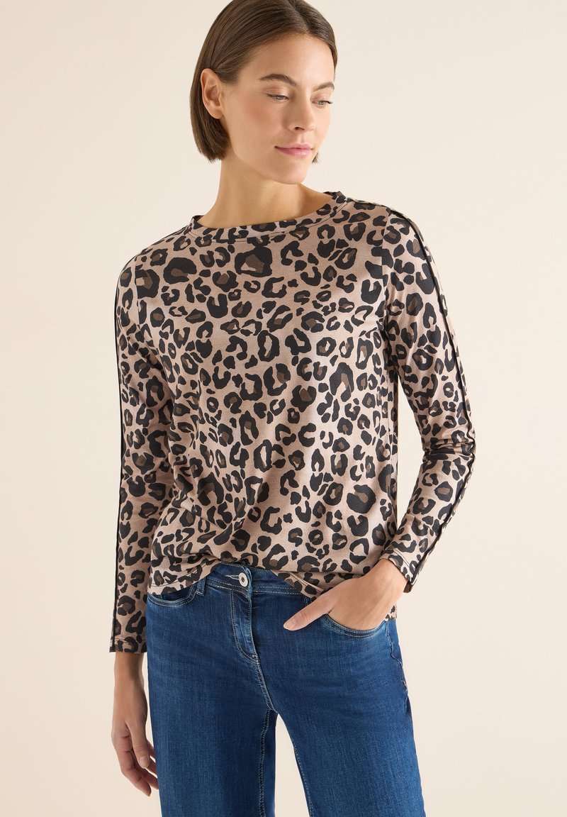 Beżowo-czarna bluzka w panterkę z długim rękawem, z okrągłym dekoltem, wykonaną z miękkiego materiału, o luźnym kroju, zestawiona z niebieskimi jeansami.
