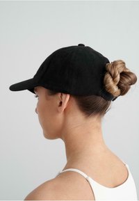 Gorra de béisbol negra con visera curvada, hecha de material suave, con un acabado texturizado. Cabello peinado en un moño trenzado en la parte de atrás.
