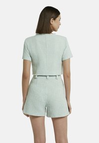 Afgekorte lichtblauwe tweed top met korte mouwen, gecombineerd met bijpassende hooggetailleerde shorts; textiel met een subtiel geweven patroon.