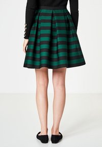 Falda a rayas verde y negra con una silueta acampanada, plisados y una tela suave. Combinada con zapatos planos negros y una camiseta de manga larga de canalé.